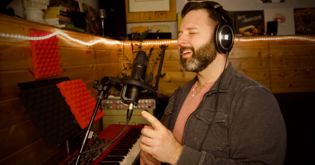 Musicien auteur compositeur interprète avec les yeux fermés chantant près de son clavier avec des lumières pour ambiance.